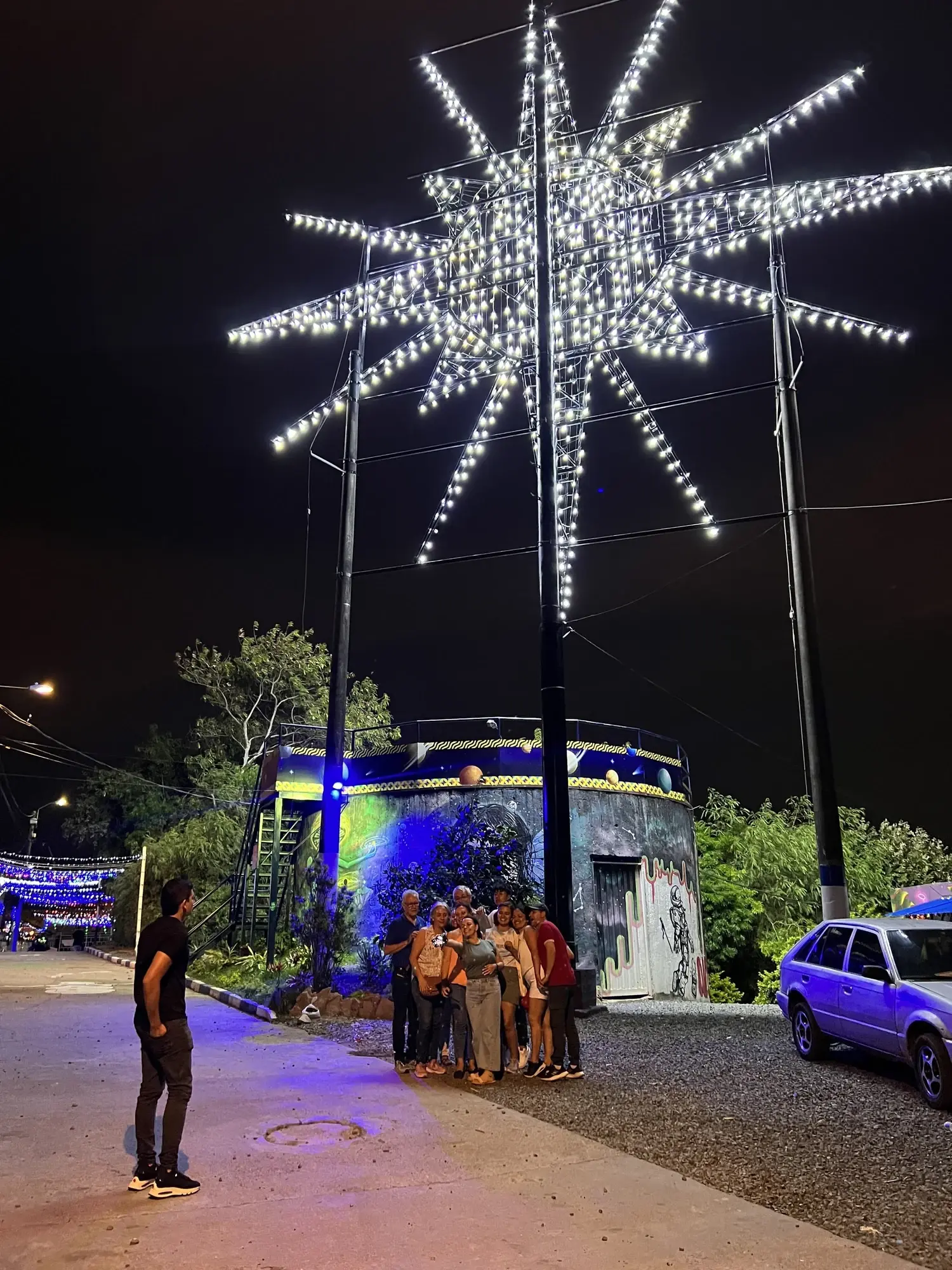 The illuminated star at the Siloé lookout in Cali at night, with a small group of visitors gathered below.